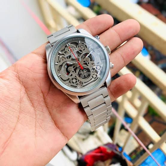 Hand holding a silver skeleton watch with a blurred background