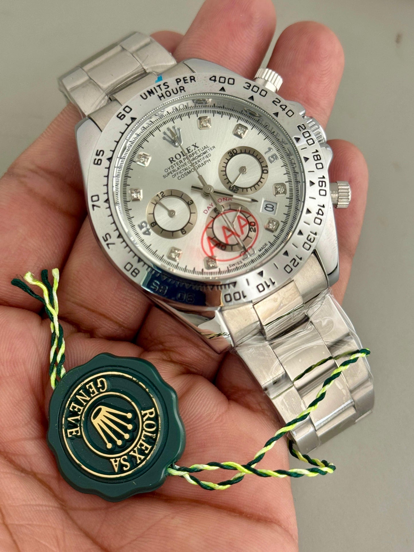 Silver Rolex watch held in a hand with a visible brand logo on a gray background