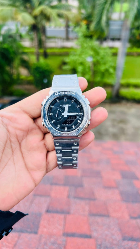 Hand holding a Casio watch with a blurred outdoor background