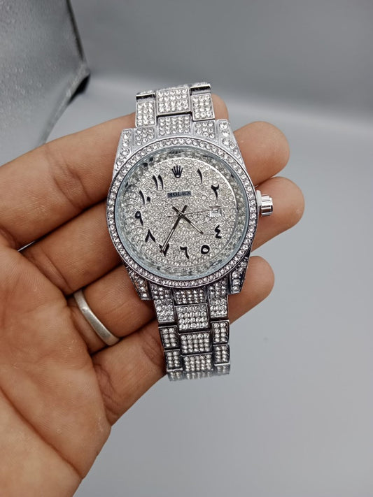 Silver diamond-encrusted watch held in a hand against a gray background