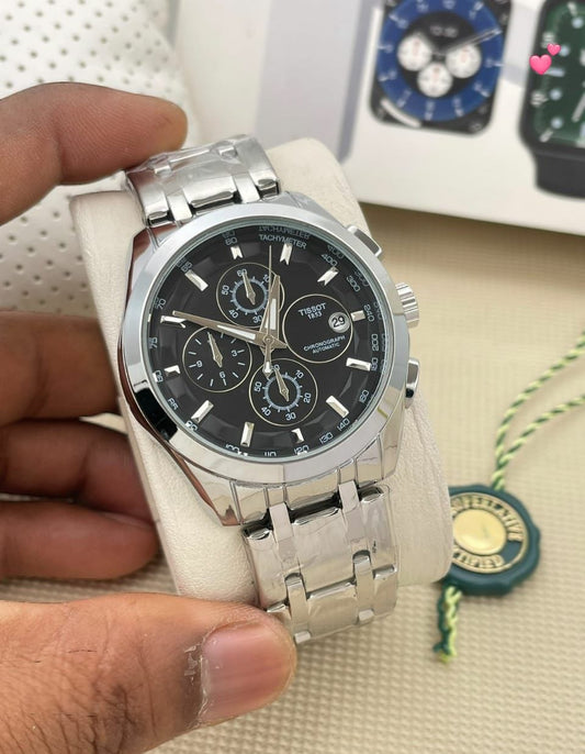 Silver watch with black face held by a hand on a textured surface.