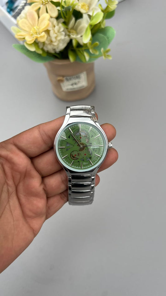 Hand holding a watch with a green face and silver case against a neutral background