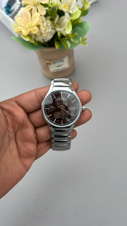 Hand holding a silver watch with a blurred background of flowers and a white surface
