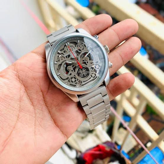 Hand holding a silver skeleton watch with a blurred background